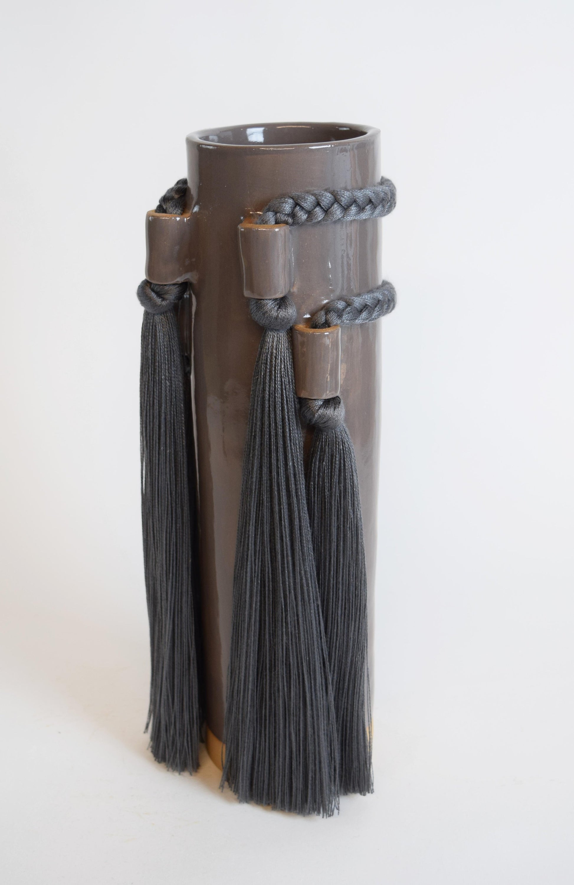A hand formed stoneware vase with elegant fringe and braided details, in a charcoal color.