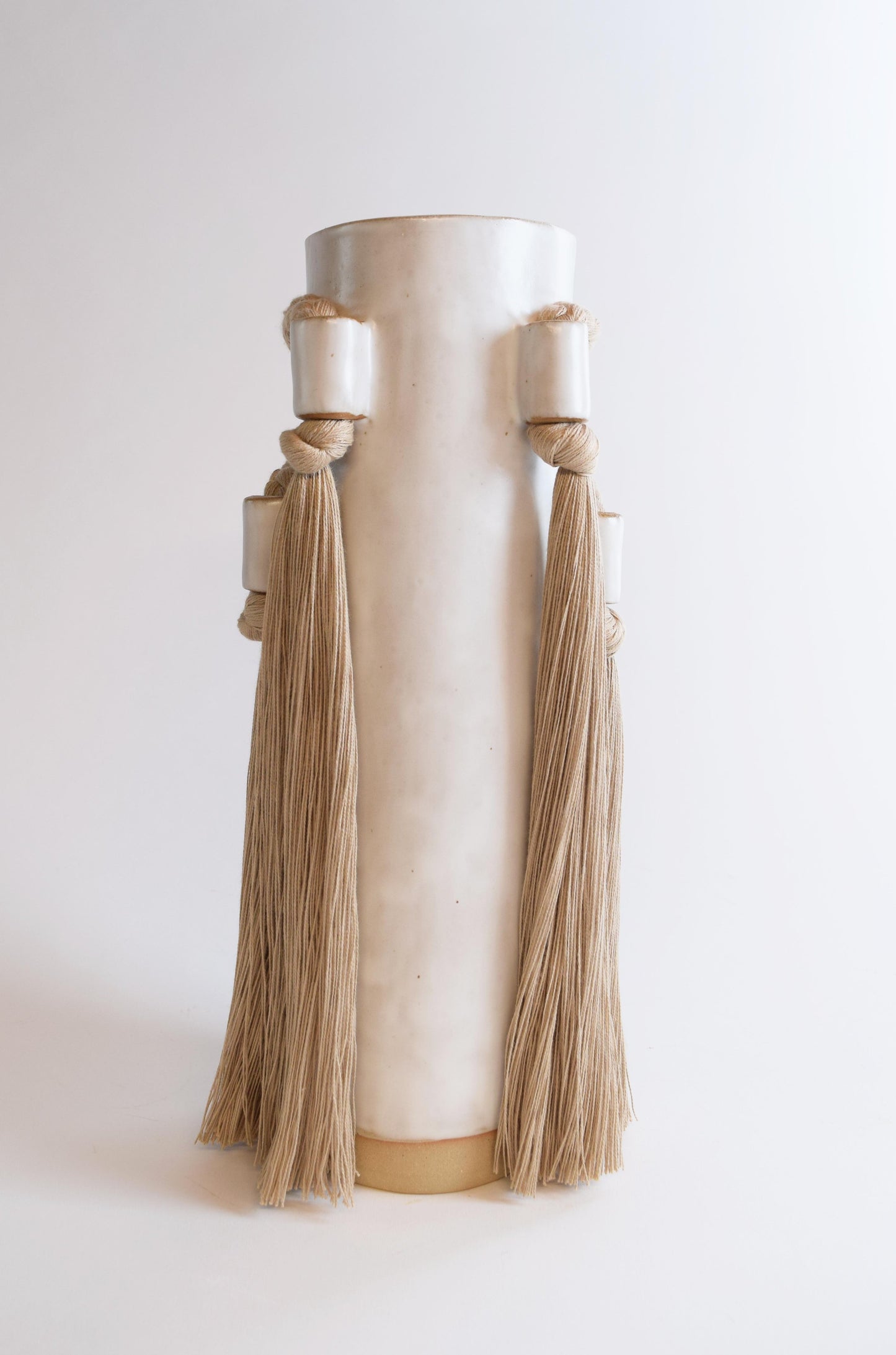 A beige stoneware vase with fringe and braided details.
