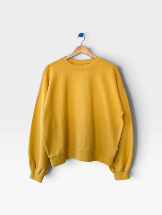 A mustard yellow crewneck sweatshirt hanging on a wooden hanger against a light gray background.