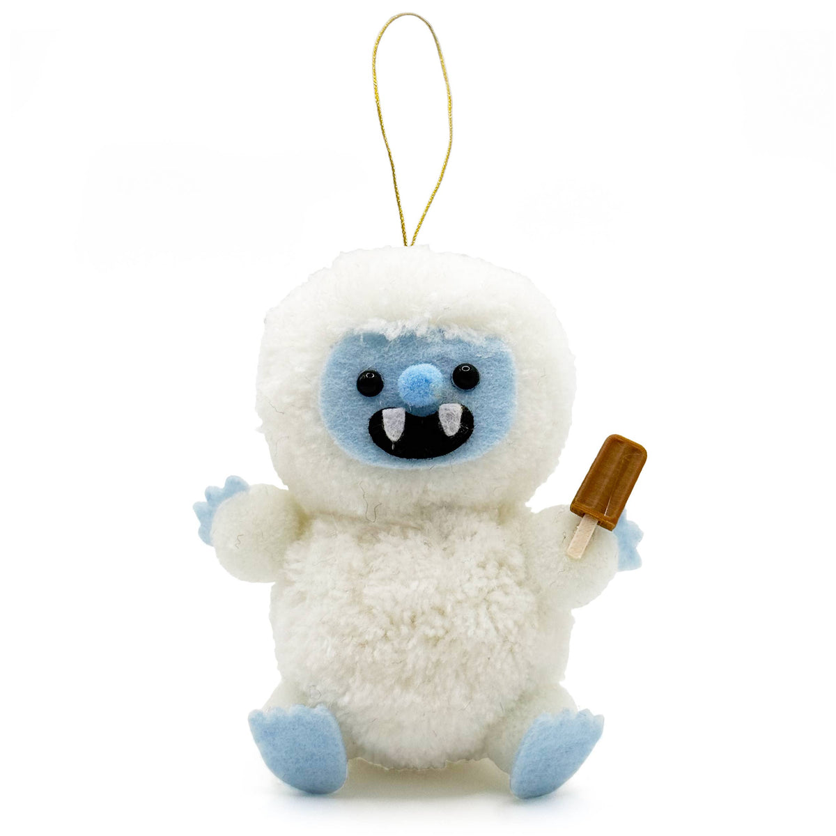A plush white yeti christmas ornament with light blue facial features, blue feet, and a gold hanging loop, holding a small brown popsicle on a plain white background.