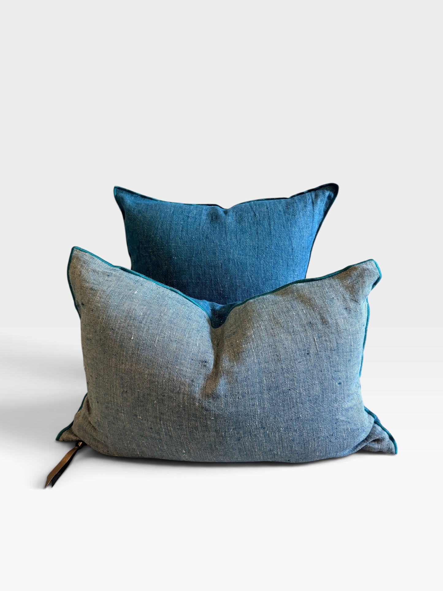 Two textured throw pillows, one in slate blue and one in a deep teal color, with matching blue piping, set against a plain light gray background.