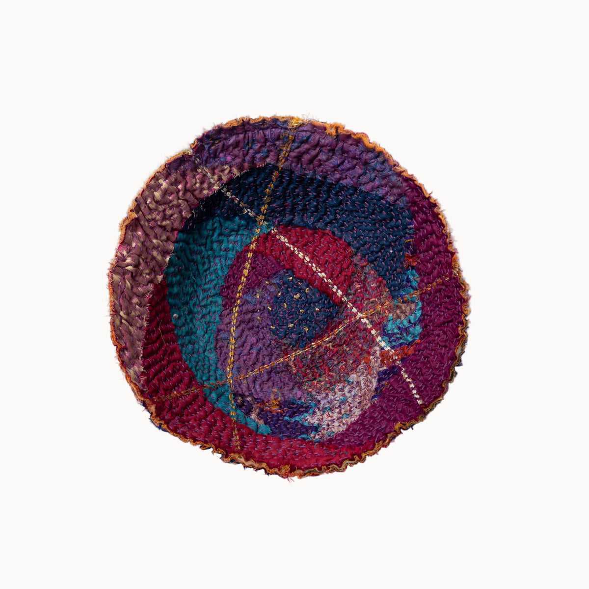 A circular handwoven rug with a textured, raised pattern in shades of purple, magenta, teal, and brown, photographed from directly above on a clean white background.