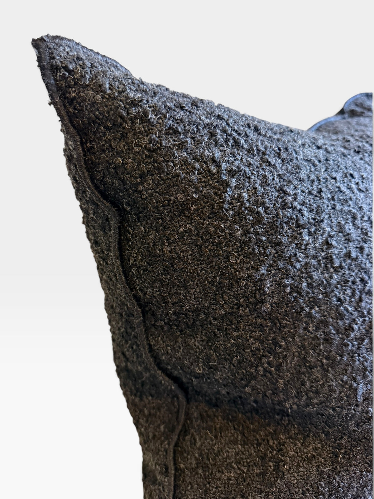 Close-up of a dark charcoal textured throw pillow with a heavily ribbed, nubby fabric surface and visible seam stitching, set against a plain light gray background.