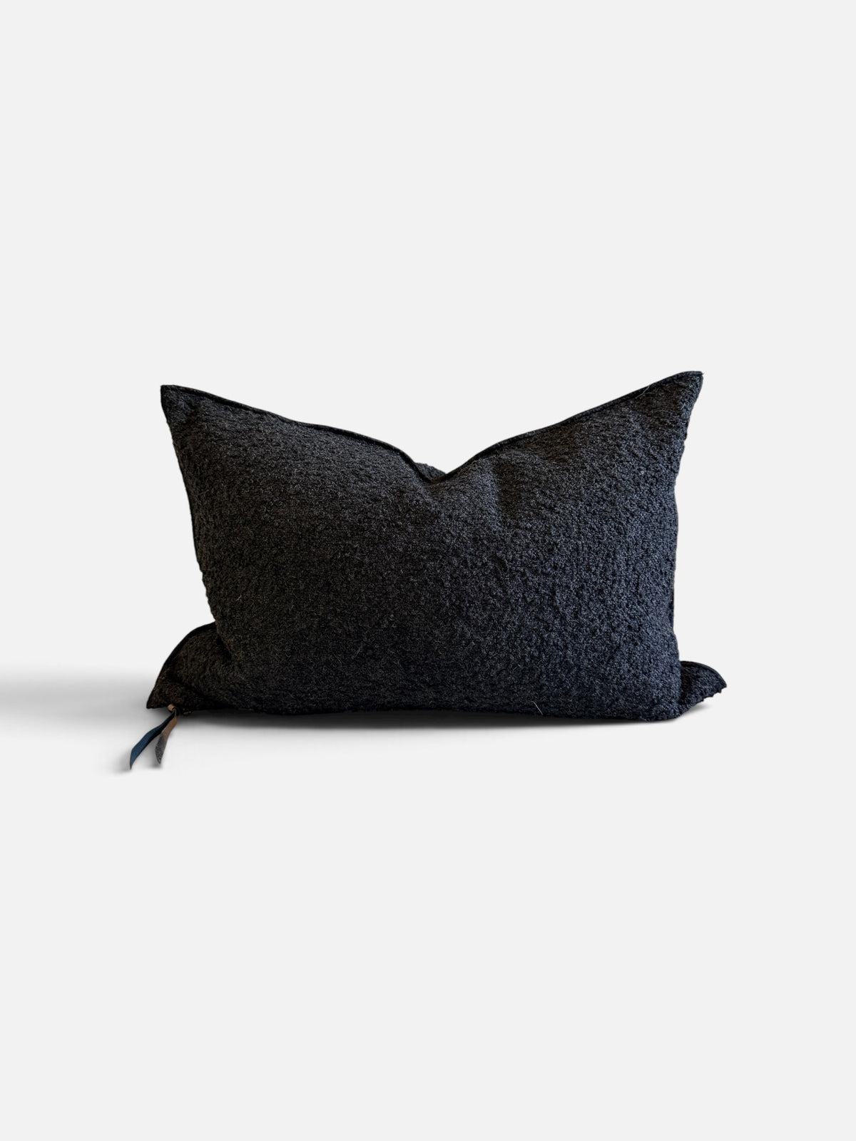 A dark charcoal textured throw pillow with a small blue and white tassel detail on the left side, photographed against a clean off-white background.