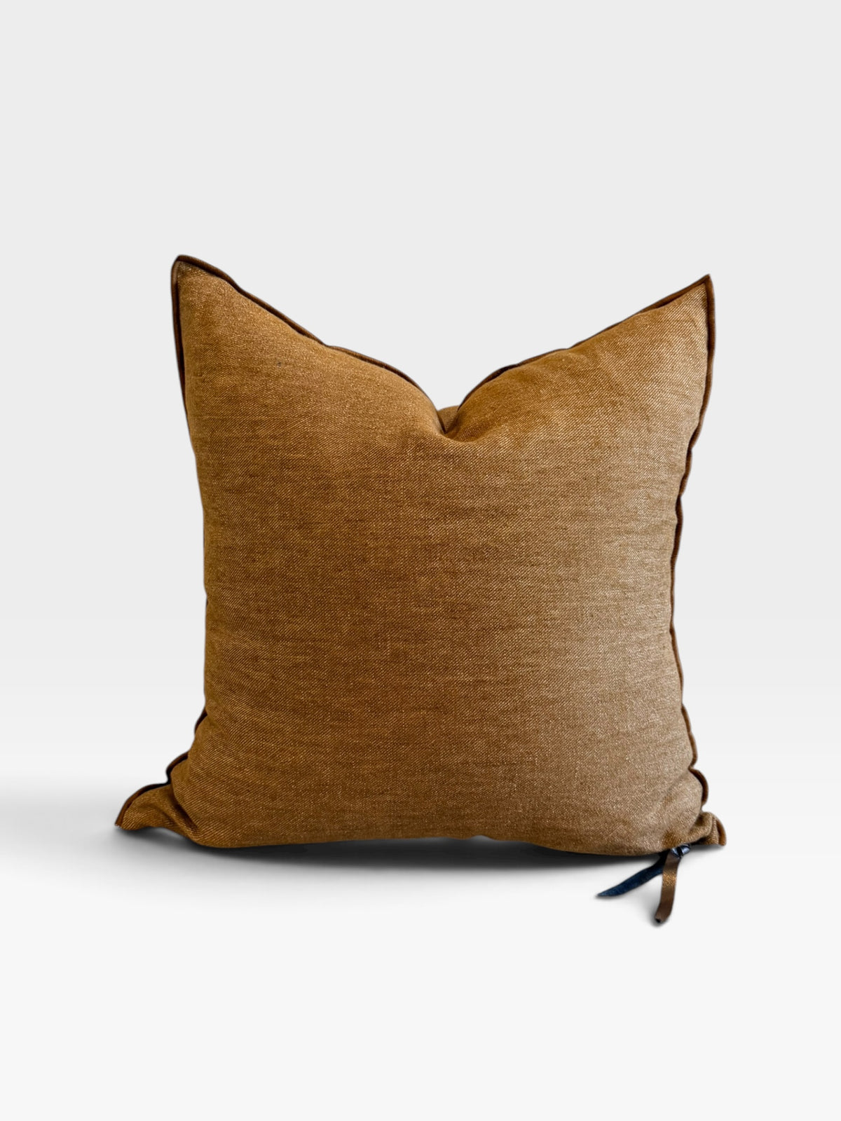 A square decorative throw pillow in a textured mustard-brown linen fabric with dark brown piped edges, shown on a clean light gray background.