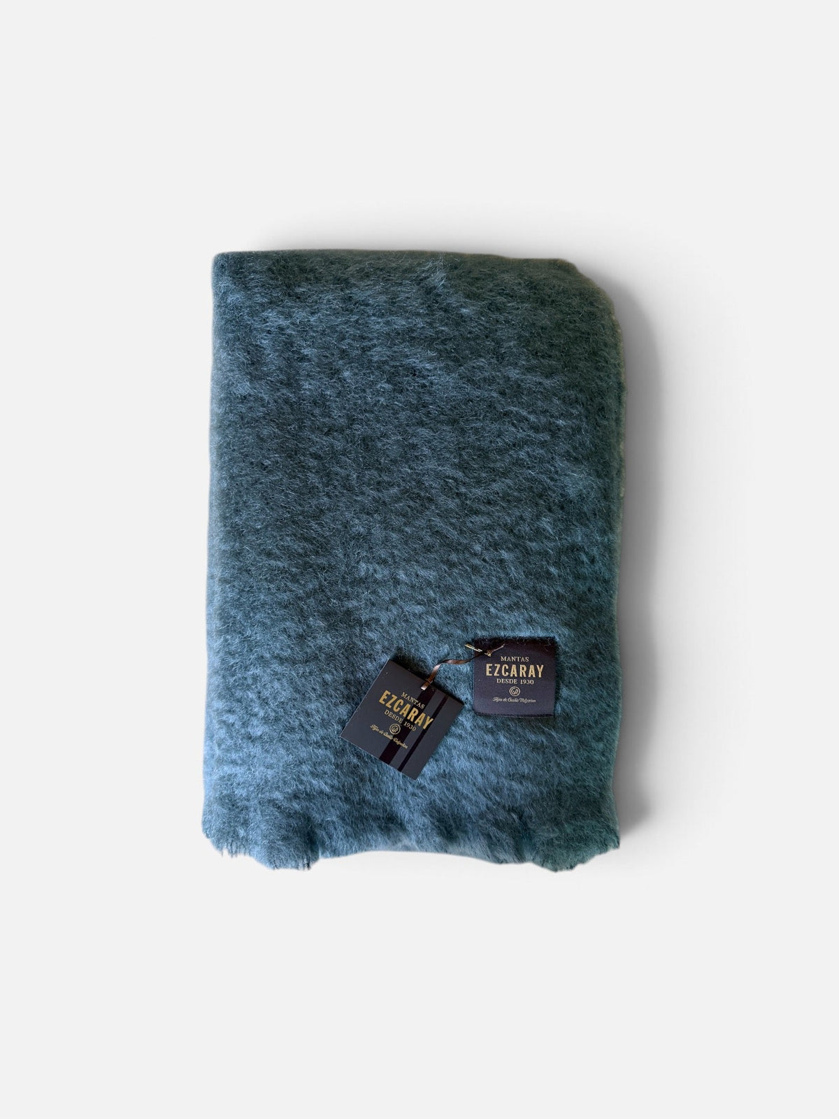 A folded dark teal blue-green fuzzy scarf with two black brand tags, displayed on a clean white background.