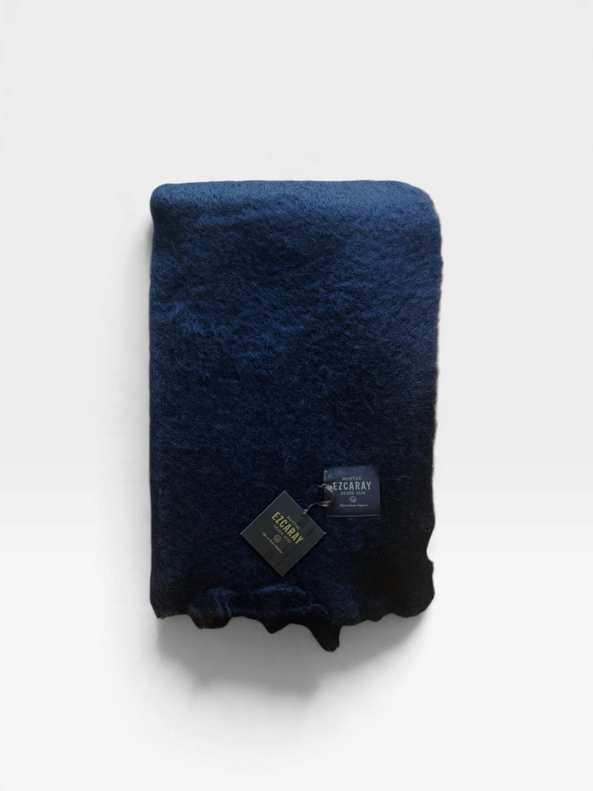 Black mohair blanket with frayed edges folded and sitting on a white background