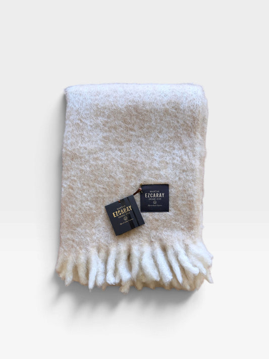 A fringed ivory mohair blanket folded and sitting on a white background
