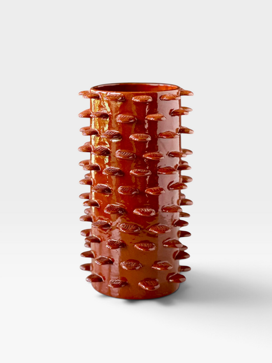 Burnt red colored ceramic vase with petal shaped detailing throughout set against a white background