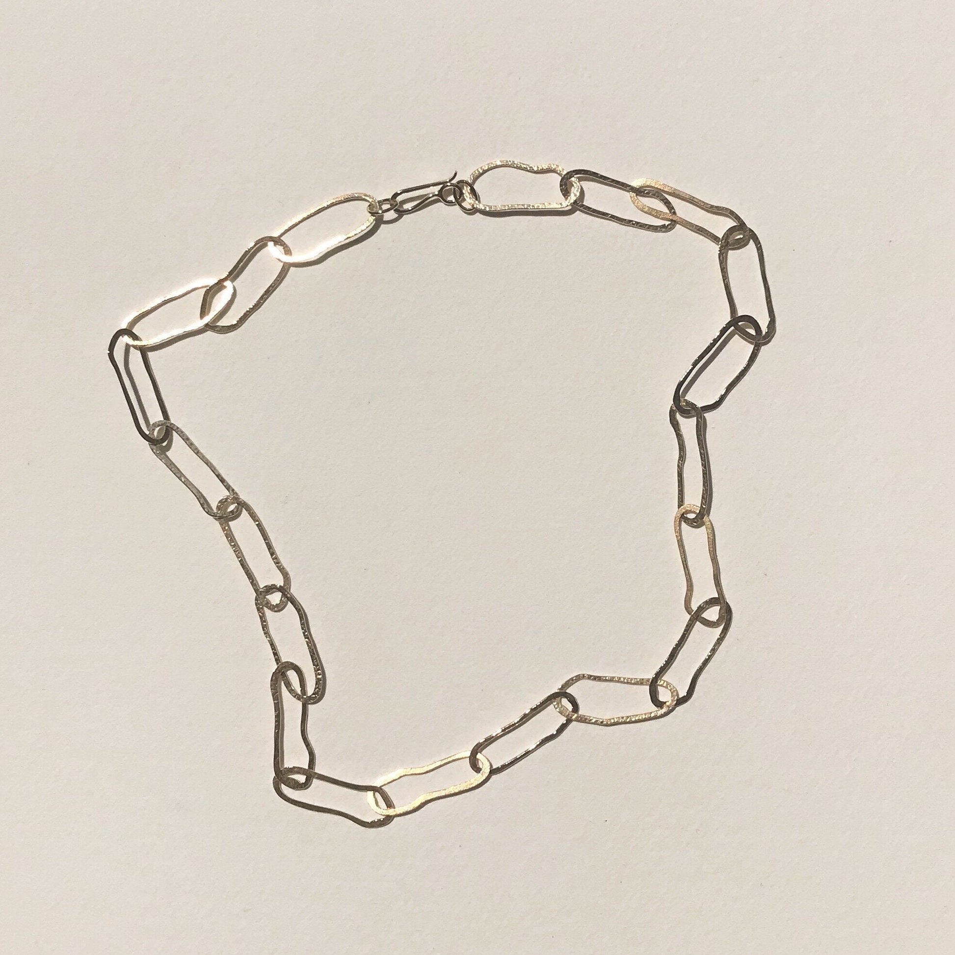 A gold chain link necklace laid out on a plain background, showing the infinity symbol shape