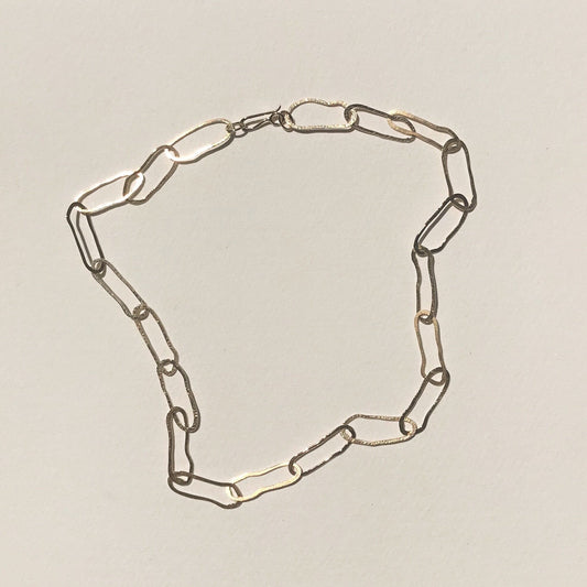 A gold chain link necklace laid out on a plain background, showing the infinity symbol shape