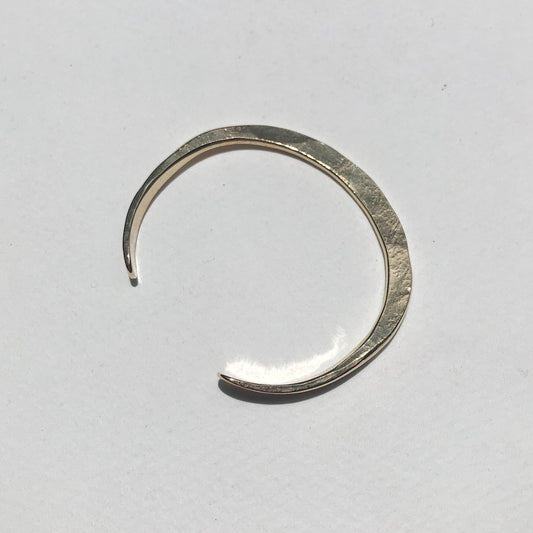 A gold cuff bracelet with a textured surface, featuring a crescent moon shape, displayed on a white background.
