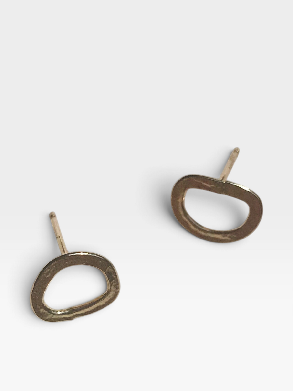 A pair of abstract oval stud earrings with a textured, hammered metallic finish in a warm bronze color, shown on a clean light gray background.