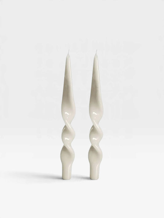 A pair of two lacquered white candles in a twisted design set against a white backdrop