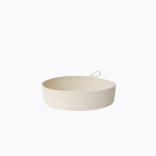 A small, round, beige rope basket with a handle, made from natural cotton, against a white background.