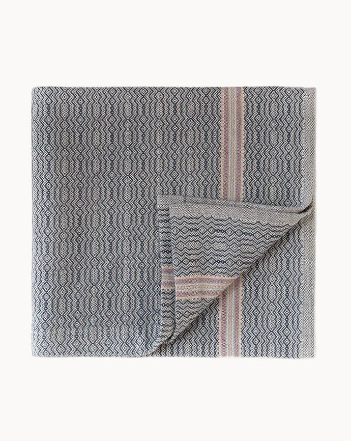 Gray patterned kitchen towel with dusty pink and dark blue accents and a folded corner on a white background