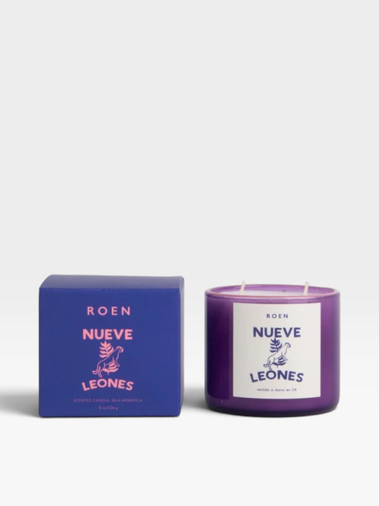 A purple wax candle in a glass jar next to its blue packaging box, both featuring the ROEN NUEVE LEONES label and design on a light gray background.