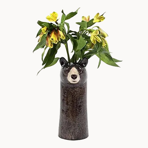A dark brown ceramic vase shaped like a bear's head, filled with yellow flowers and green leaves, set against a plain white background.