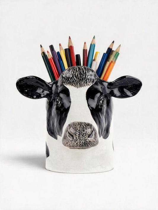 A ceramic cow head pencil holder with a glossy black and white painted finish, filled with various colored pencils on a clean white background.