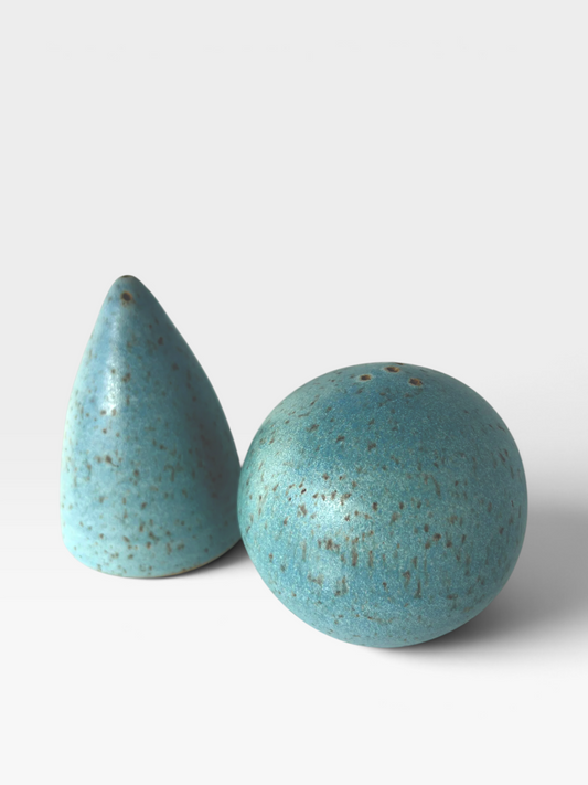 A set of speckled teal-colored ceramic salt and pepper shakers with one shaker in a spherical shape and the other in a rounded conical shape set against a white background