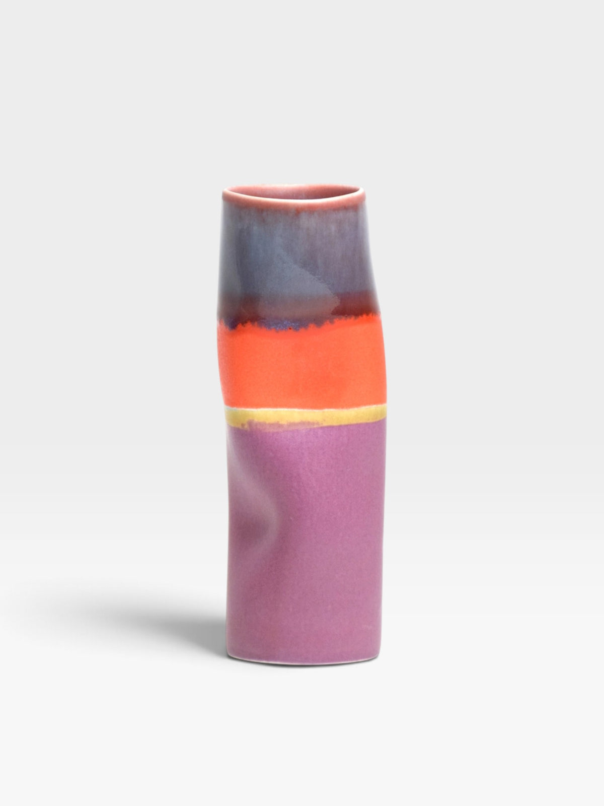A cylindrical vase with a a multi-colored glaze in pink, blue, orange, yellow, and purple hues set against a light gray background. 