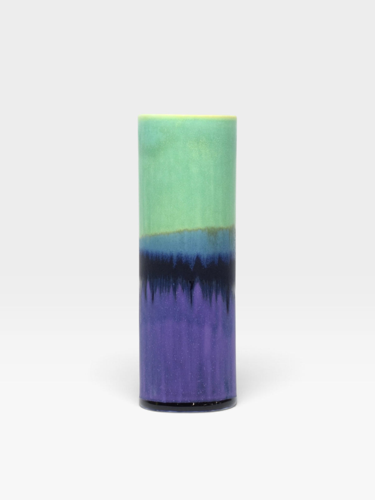 A cylindrical vase with a a multi-colored glaze in green, blue, and purple hues set against a light gray background. 