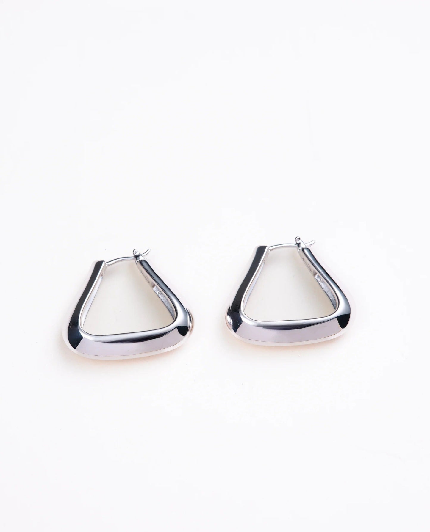 Triangle shaped silver hoop earrings on a pale gray background