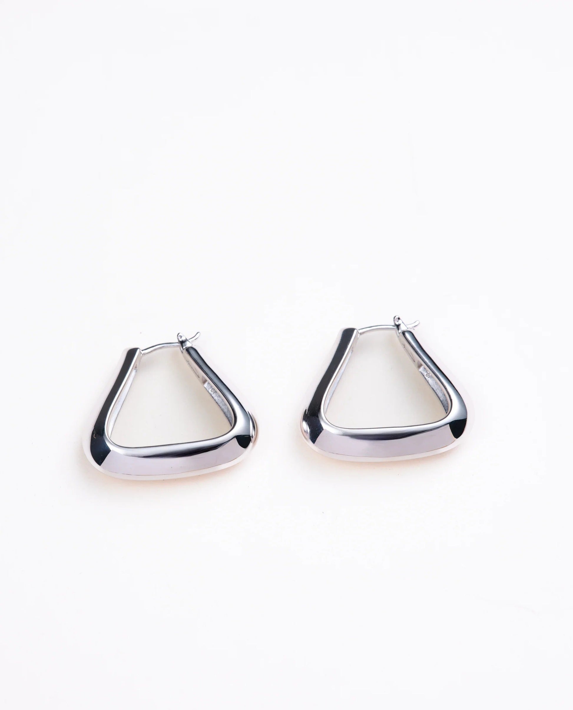 Triangle shaped silver hoop earrings on a pale gray background