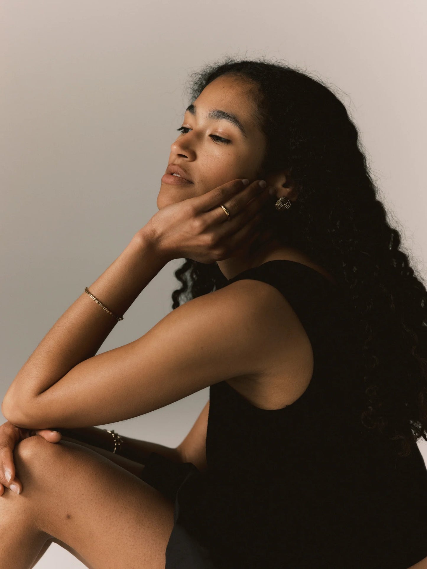 Woman sitting with hand on face against a neutral background