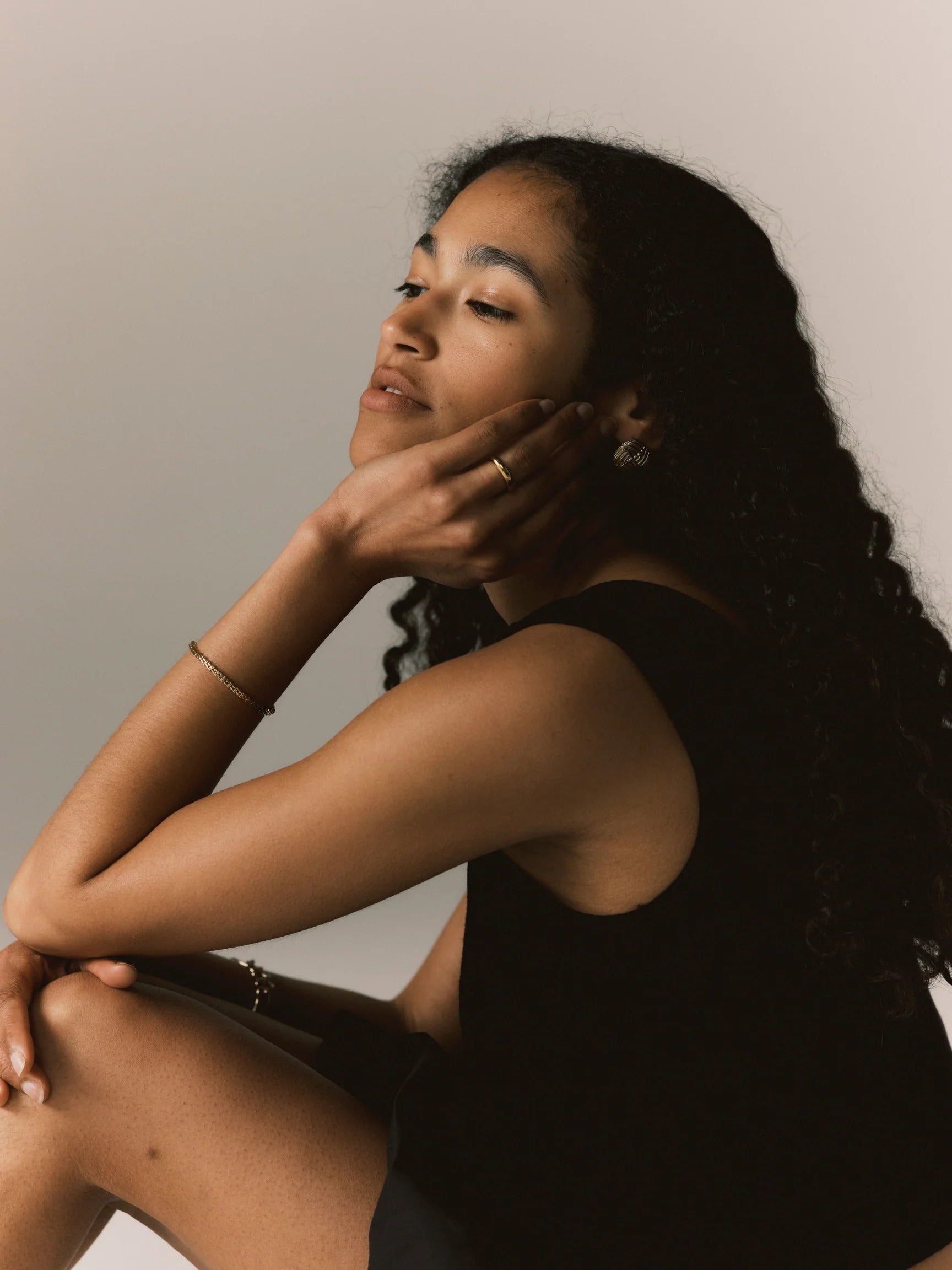 Woman sitting with hand on face against a neutral background