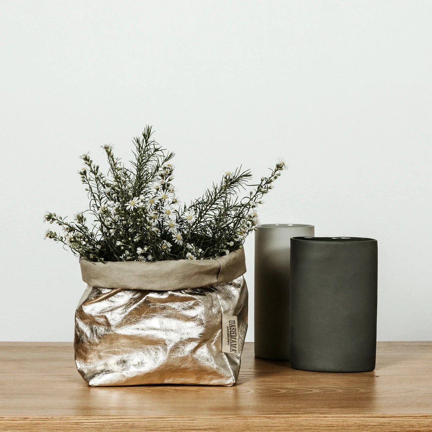 Gold metallic bag with plants on a wooden surface next to two dark gray vases.