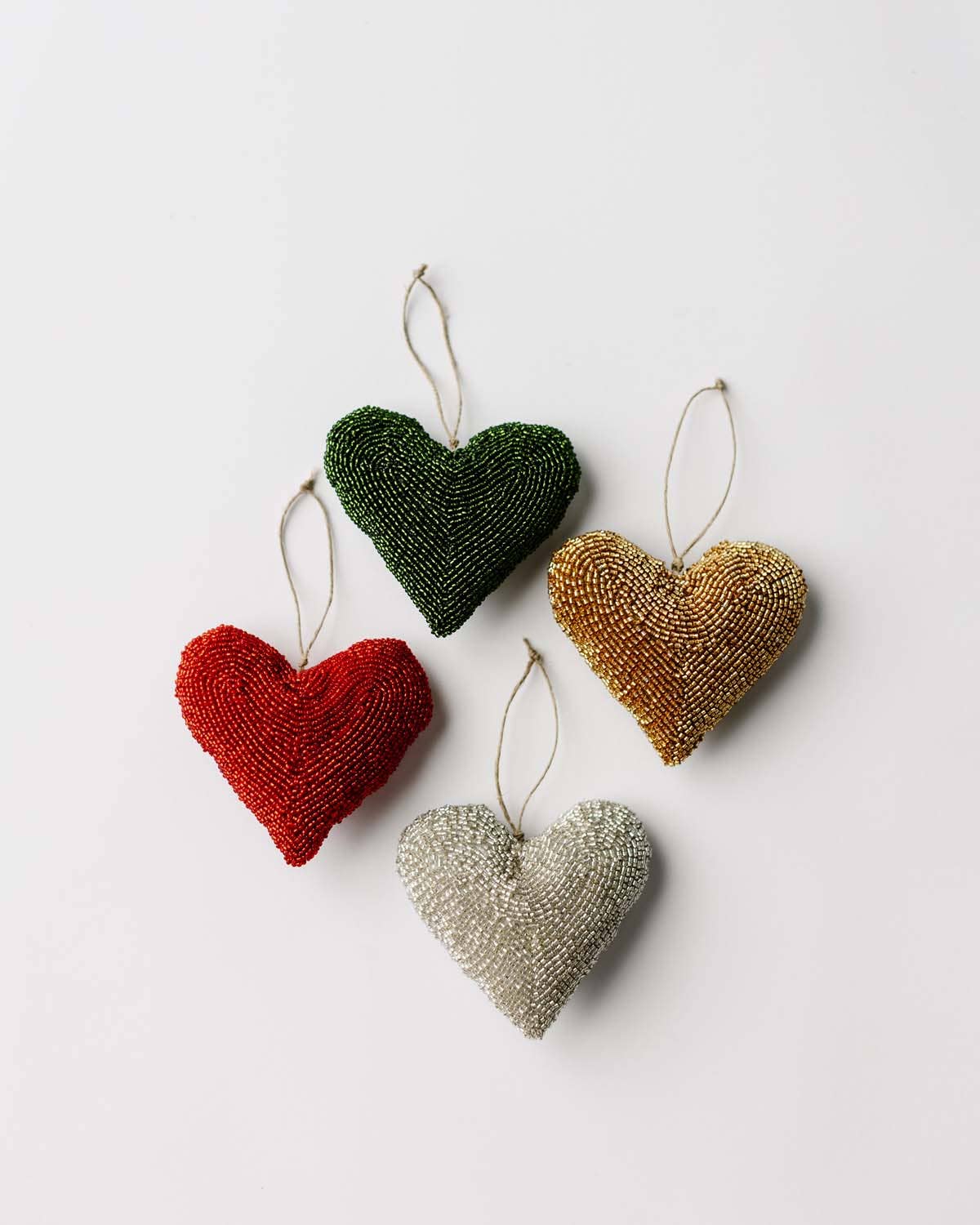 Four heart-shaped beaded ornaments in red, green, gold, and silver on a white background