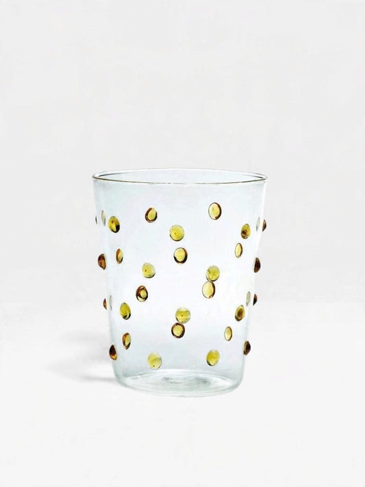 A clear glass tumbler decorated with scattered metallic golden polka dots, photographed against a seamless white background.