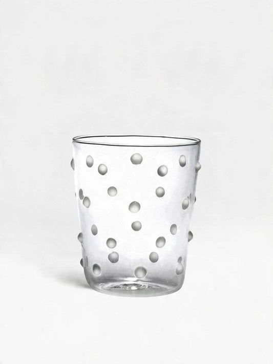 A clear glass tumbler with a pattern of raised, beaded white dots, photographed against a seamless light gray background.