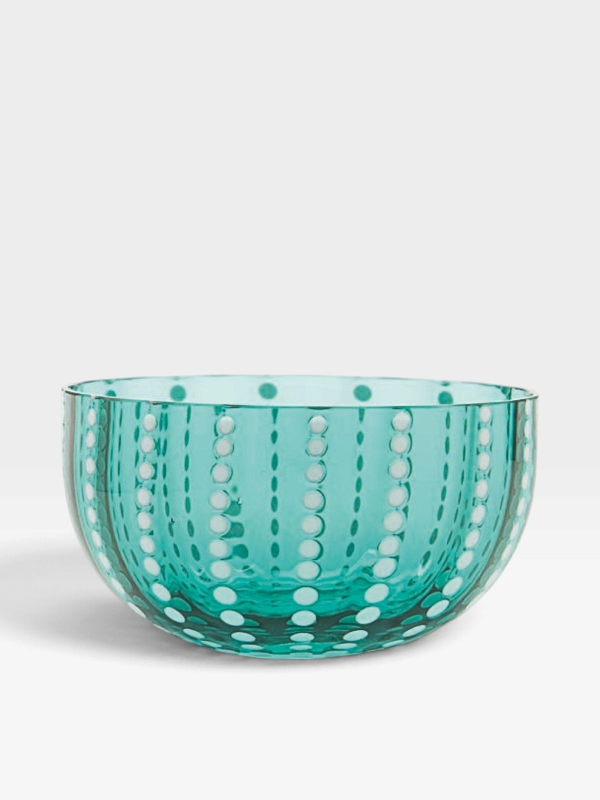 A translucent glass bowl in a teal color with a pattern of white dots sitting against a white background