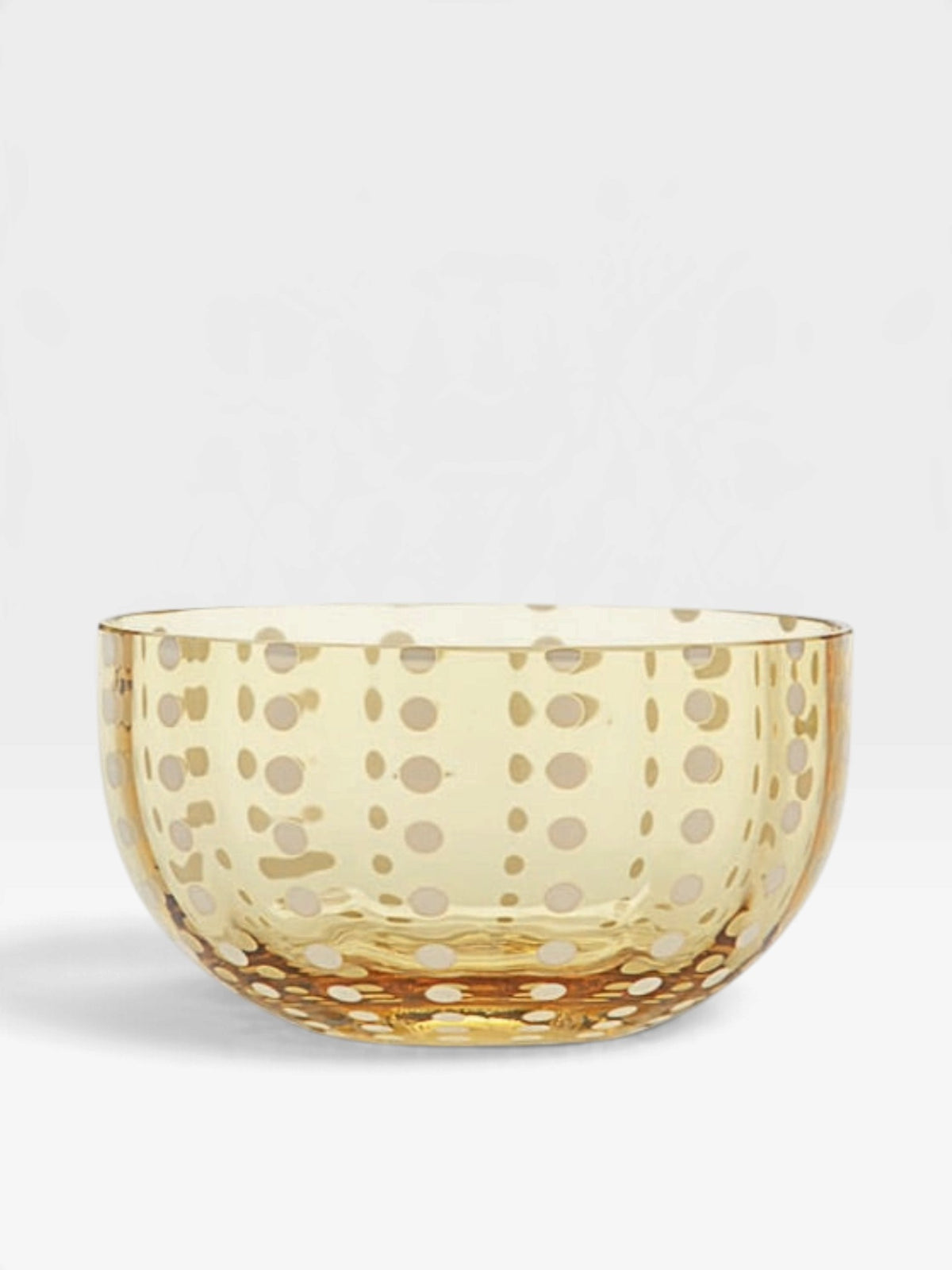 A translucent amber glass bowl decorated with a pattern of white dots, set against a clean white background.