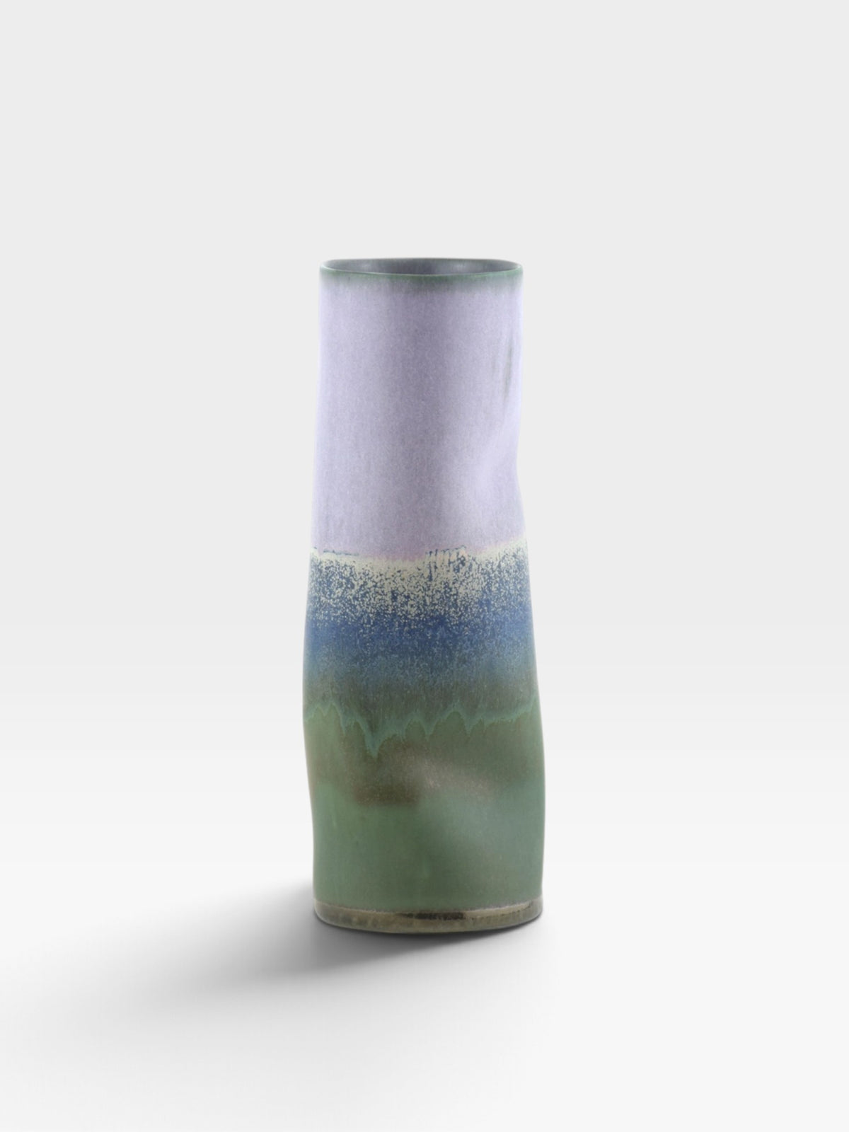 A cylindrical vase with a a multi-colored glaze in green, blue, and lavender hues set against a light gray background. 