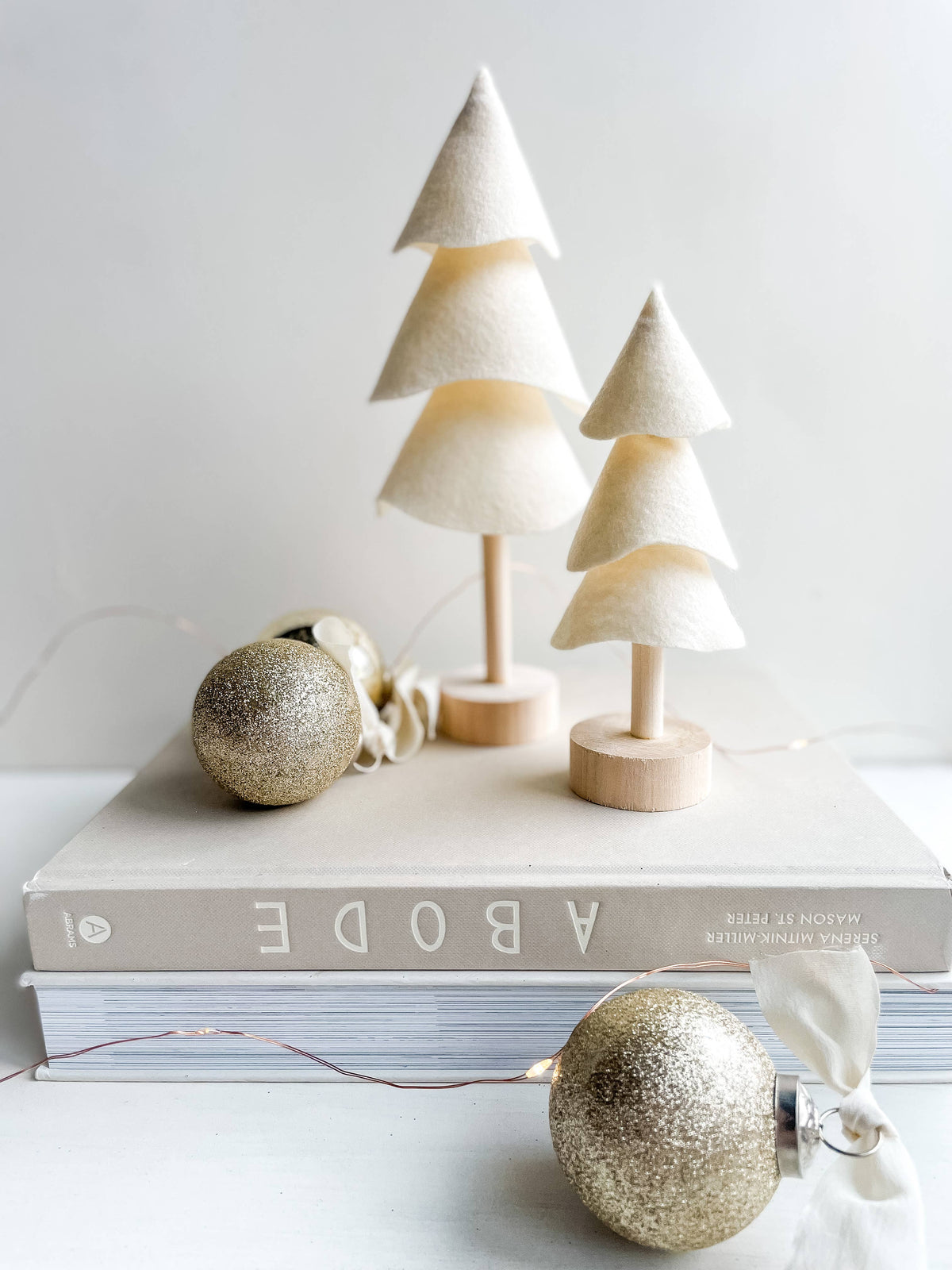 Ivory felt Christmas trees on a washed wood base sit on a book with decorative holiday ornaments
