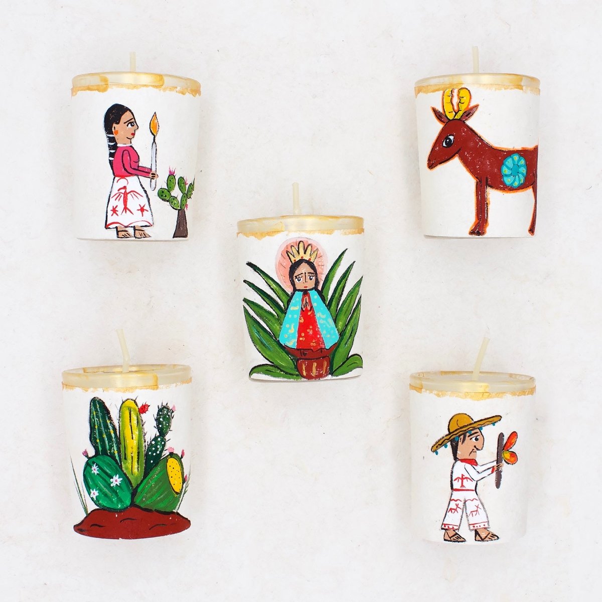 A collection of six handpainted votive candle holders, each with a unique folk art design, including representations of a person, a deer, a cactus, and other symbols related to Mexican culture.