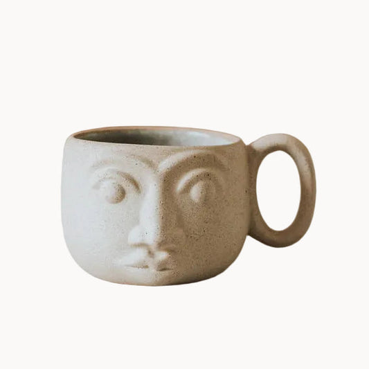 Ceramic mug with face design on a neutral background