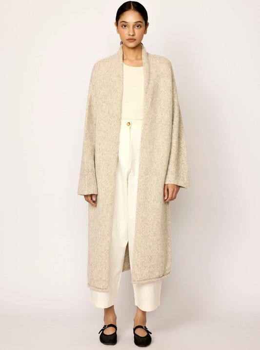 Woman wearing a beige long sweater coat over a white outfit on a plain background