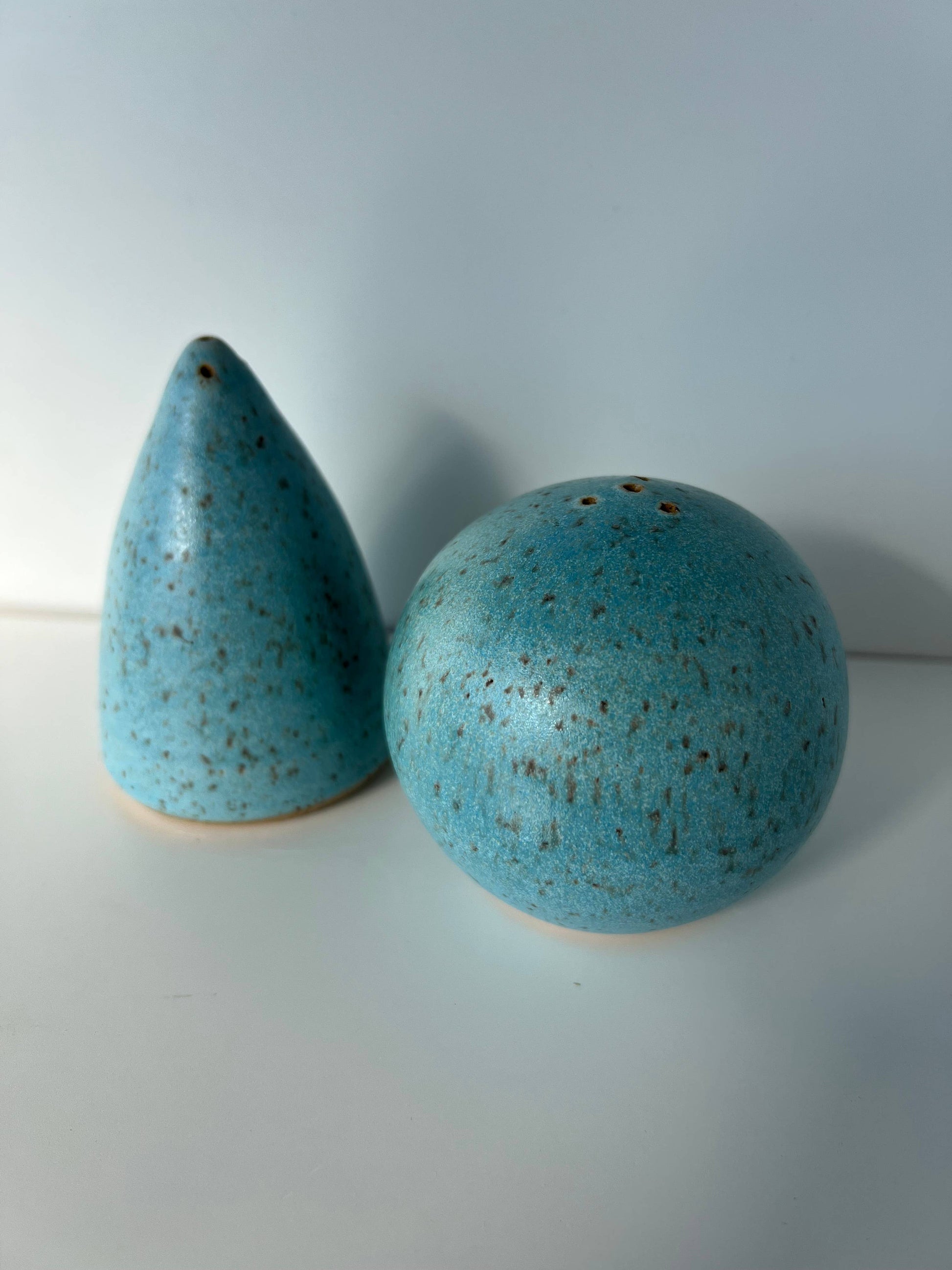 A blue ceramic salt shaker with a rounded shape and a pepper shaker with a conical shape, both with a speckled texture.
