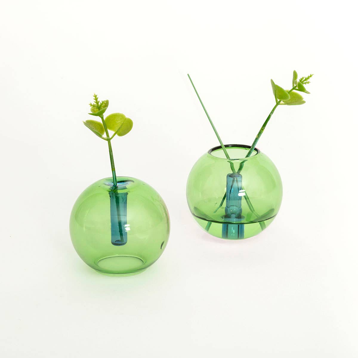 Two green and blue mini bubble glass vases on a white background, one with a single stem plant, the other with no plant.