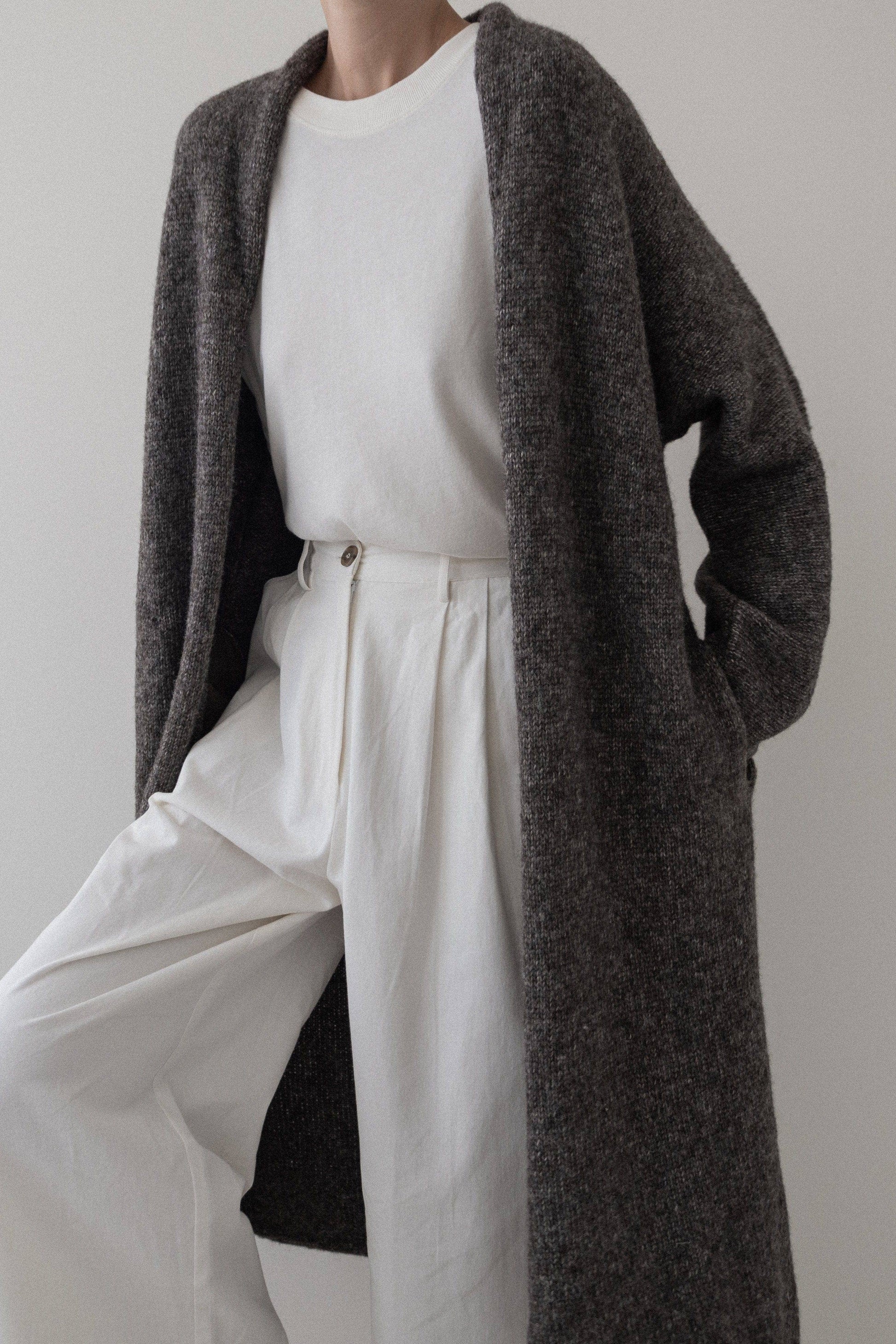 Person wearing a long dark brown cardigan over a white outfit against a plain background
