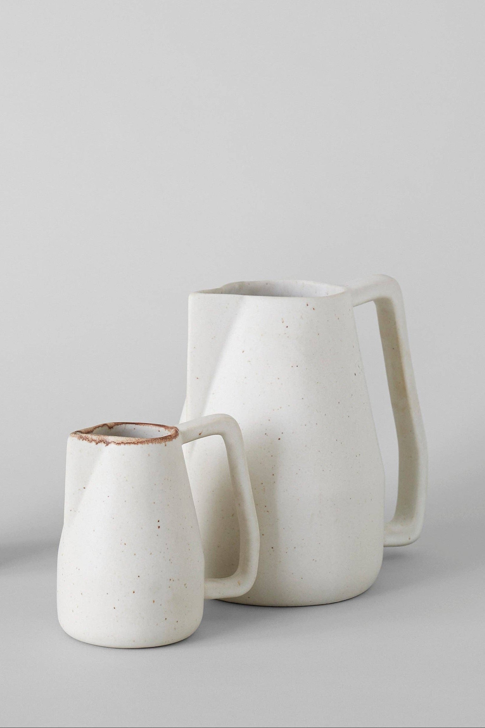 A small and large matte ivory ceramic pitcher with a soft geometric design, displayed against a neutral background