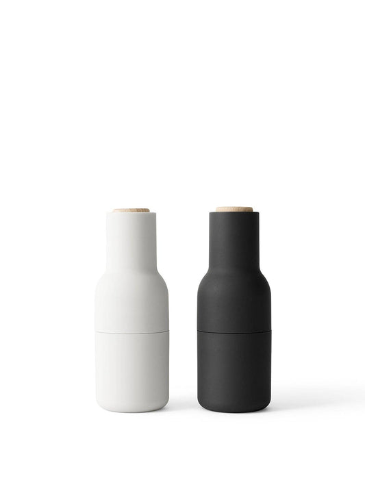 Two spice bottle grinders, one in white (Ash) and one in black (Carbon), with beech wood lids on a white background