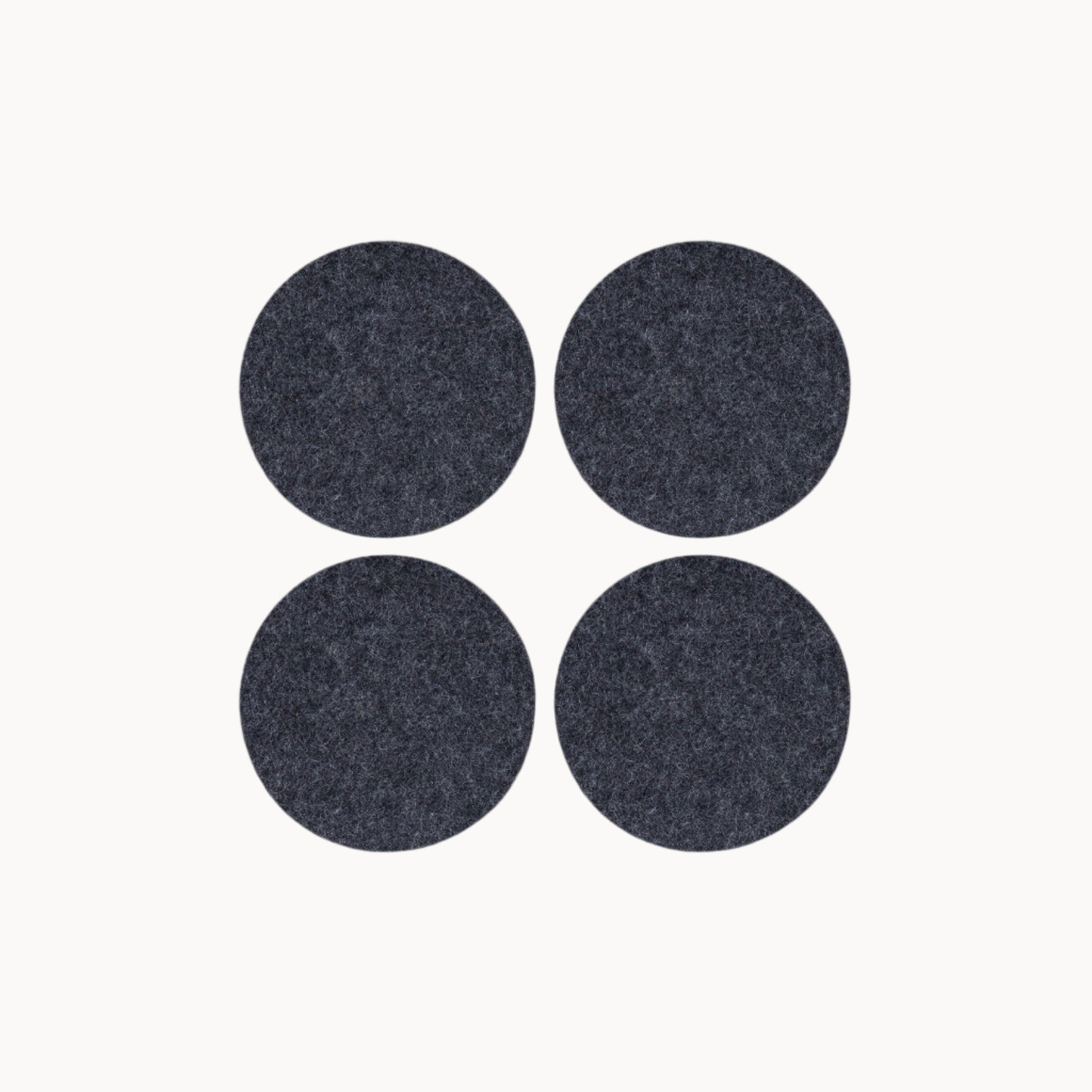Four dark gray round wool felt coasters on a white background