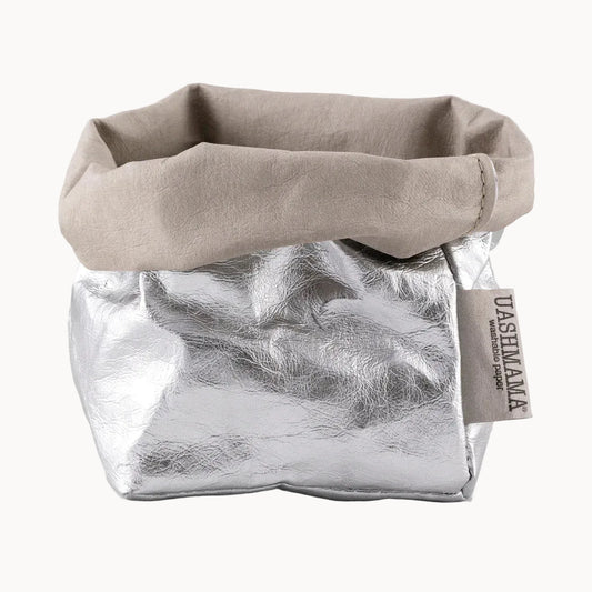 Fabric bag with a textured silver exterior and beige fabric top on a white background, featuring a brand tag.