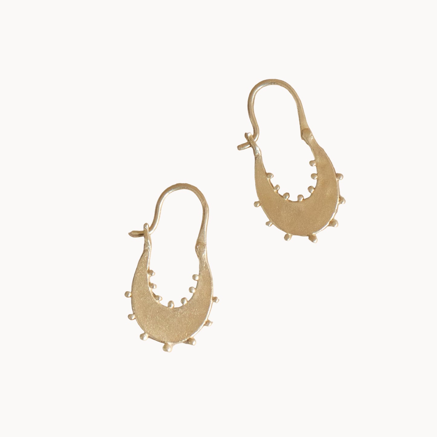 Gold hoop earrings with delicate beading on a beige background
