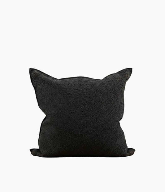 A black textured throw pillow with cat-ear points, resting on a white surface against a plain off-white background.